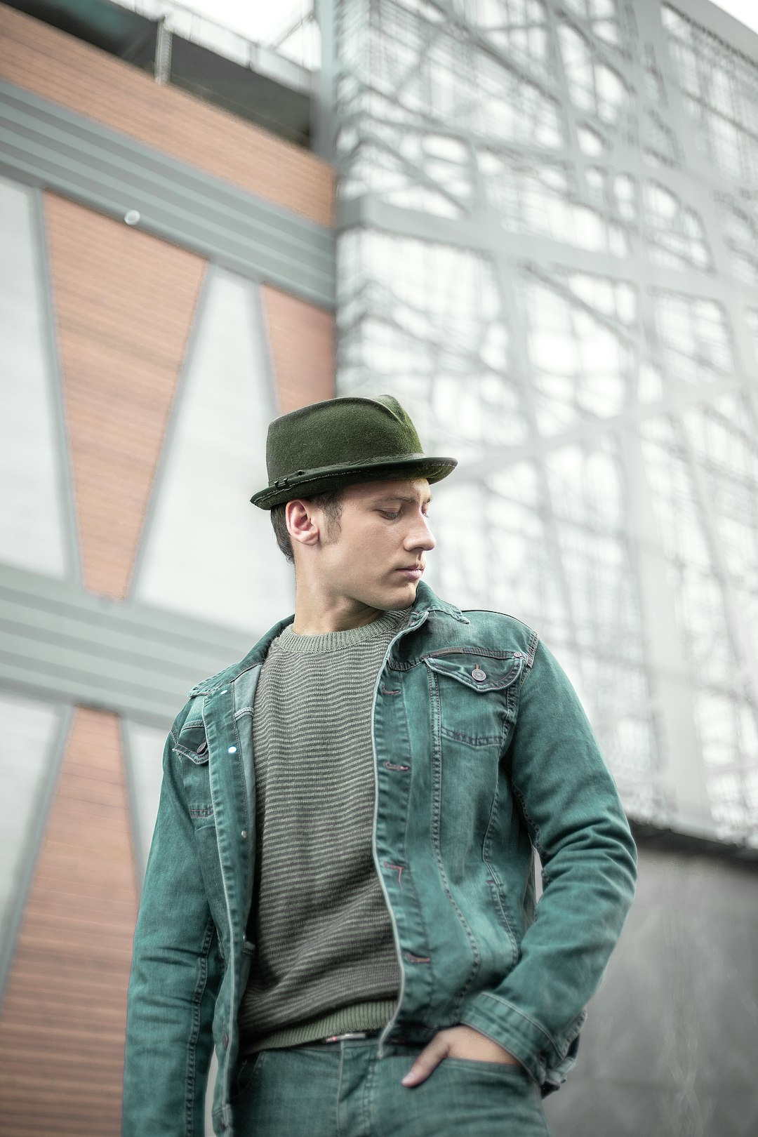 a-man-in-a-green-jacket-and-hat-standing-in-front-of-a-building-2xbae7odkh8